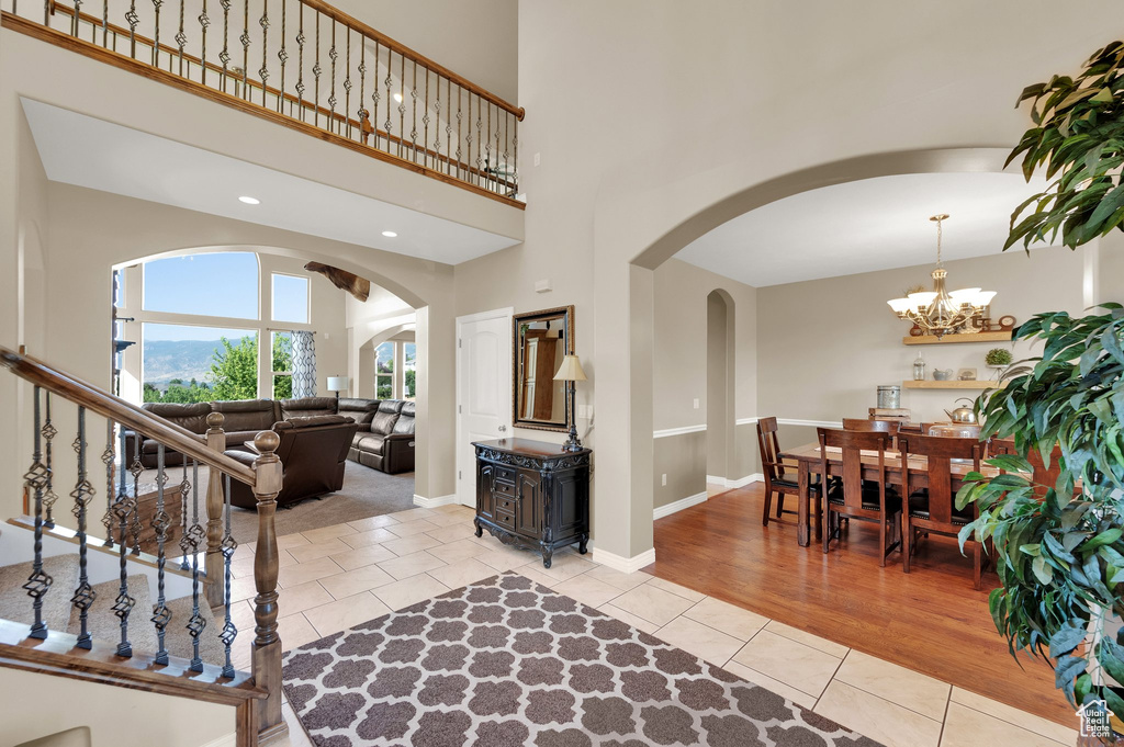 Foyer featuring arched walkways, light tile patterned floors, a chandelier, a towering ceiling, and stairway