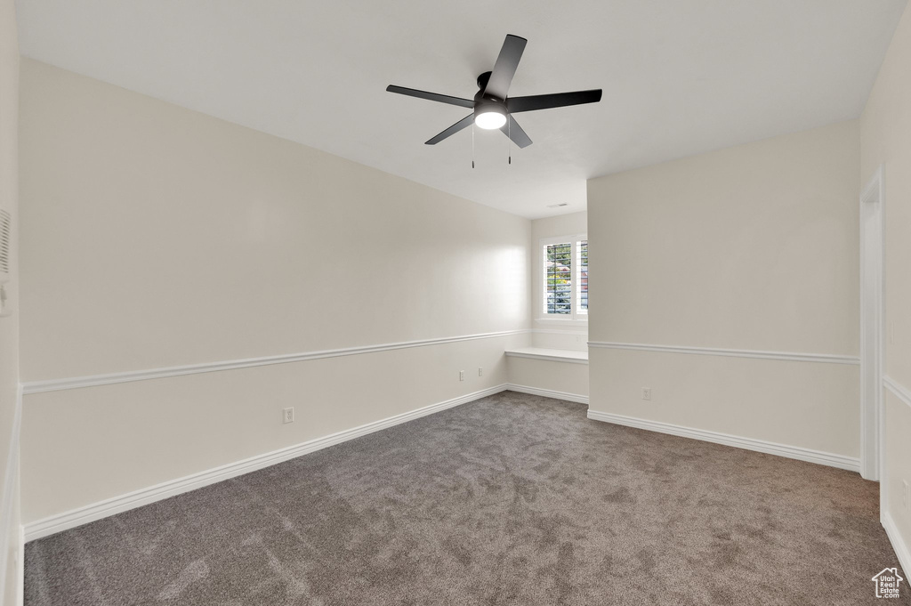 Carpeted spare room featuring ceiling fan and baseboards