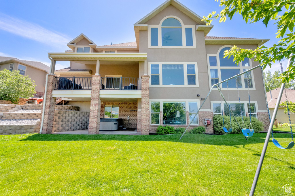 Back of house with stucco siding, a hot tub, a balcony, and brick siding