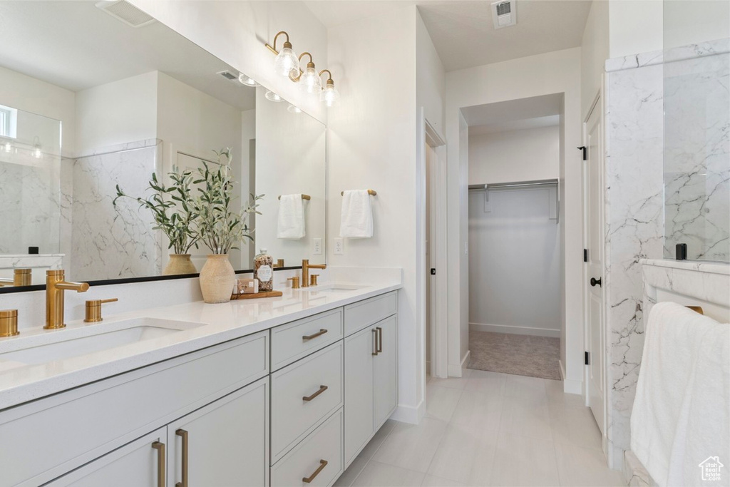 Bathroom with double vanity, a walk in closet, and a marble finish shower