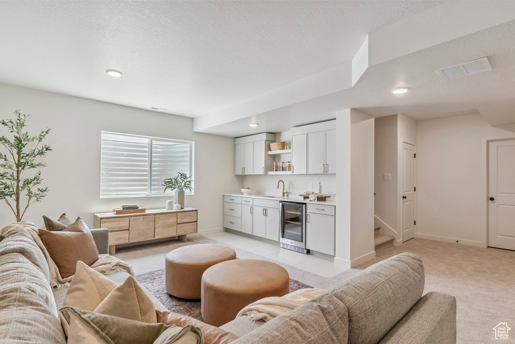 Living room featuring bar with sink, light carpet, beverage cooler, a textured ceiling, and recessed lighting