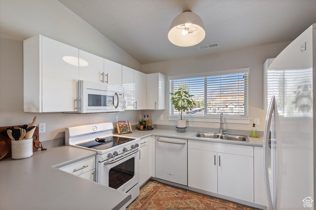 Kitchen featuring white appliances, light countertops, vaulted ceiling, and white cabinets