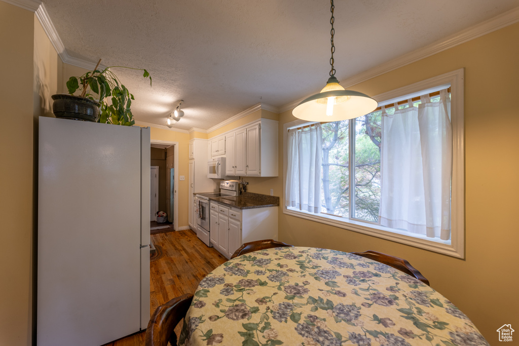Kitchen featuring white appliances, ornamental molding, white cabinets, wood finished floors, and dark countertops