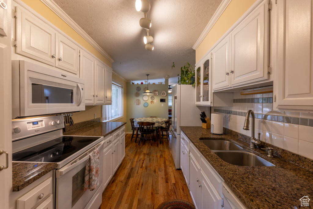 Kitchen featuring white appliances, white cabinetry, wood finished floors, a textured ceiling, and tasteful backsplash