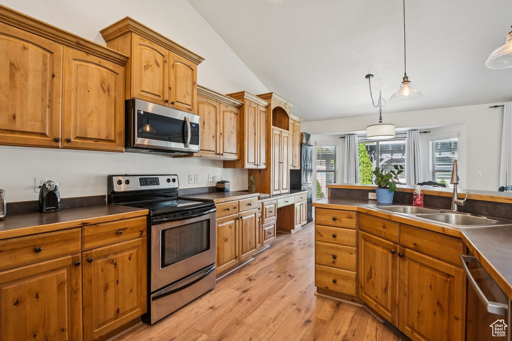 Kitchen with appliances with stainless steel finishes, dark countertops, light wood-style floors, brown cabinetry, and vaulted ceiling