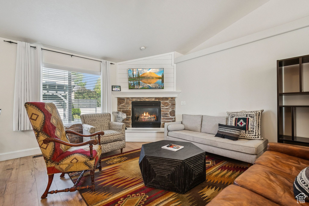 Living room with lofted ceiling, hardwood / wood-style floors, and a stone fireplace