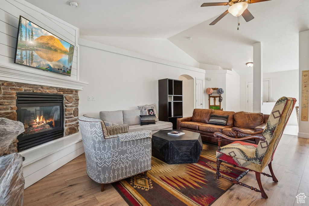 Living area with lofted ceiling, a ceiling fan, wood finished floors, a stone fireplace, and arched walkways