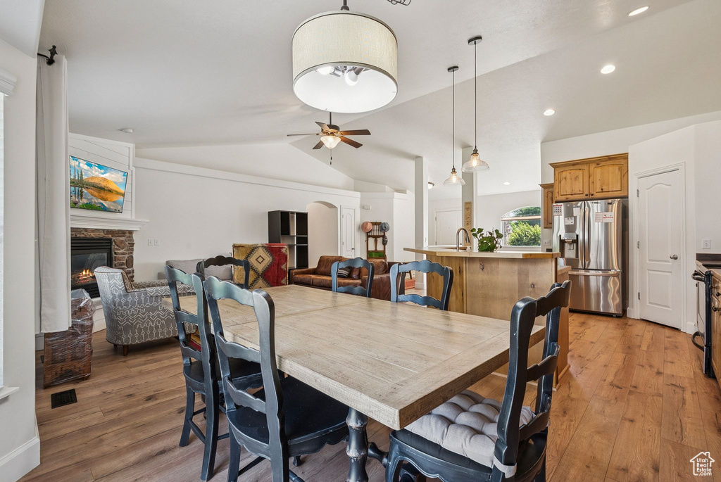 Dining area featuring vaulted ceiling, a stone fireplace, light wood finished floors, ceiling fan, and recessed lighting