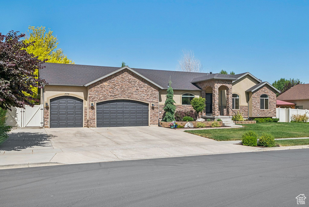 French provincial home with an attached garage, stone siding, concrete driveway, stucco siding, and a gate
