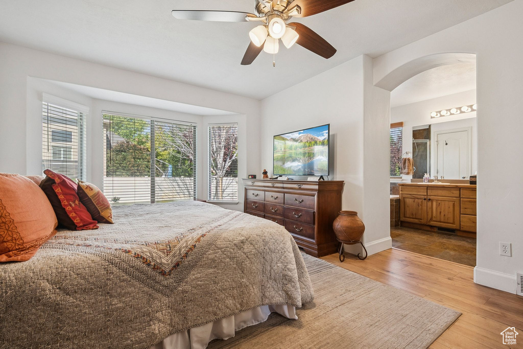 Bedroom featuring arched walkways, light wood-style flooring, connected bathroom, and ceiling fan