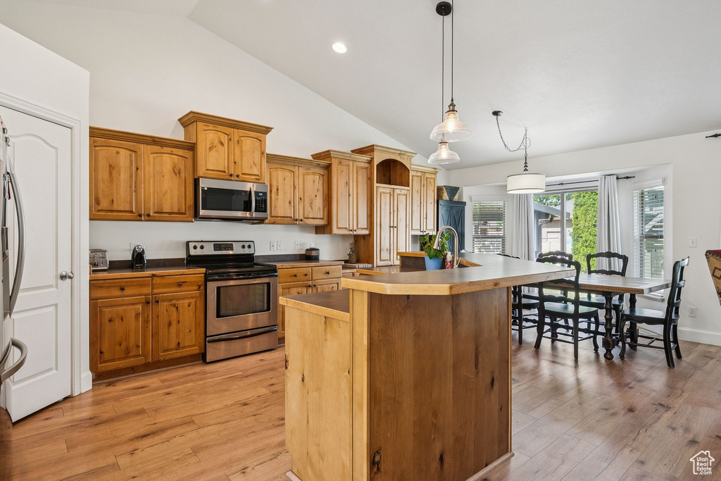 Kitchen with appliances with stainless steel finishes, an island with sink, high vaulted ceiling, pendant lighting, and light wood-style floors