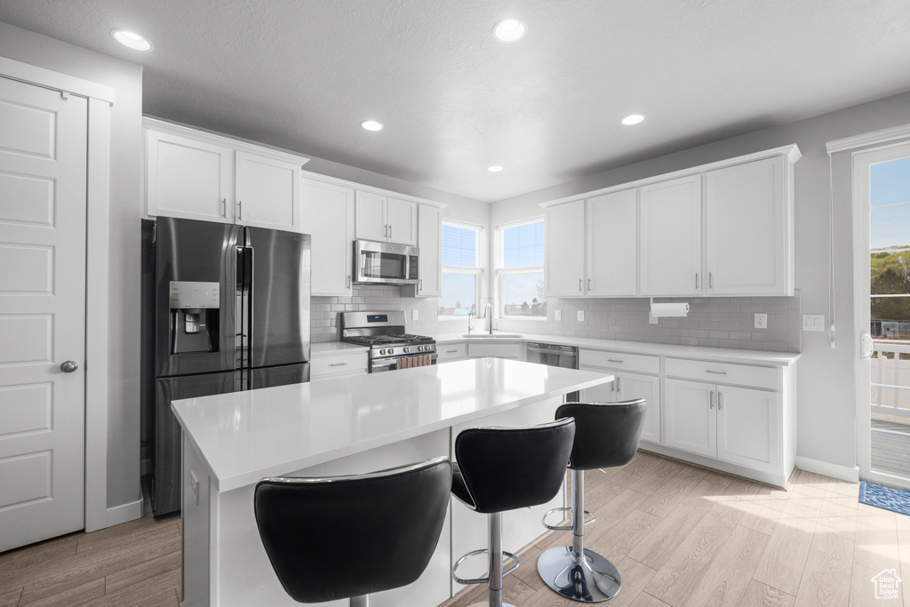 Kitchen with appliances with stainless steel finishes, backsplash, light wood finished floors, white cabinetry, and recessed lighting