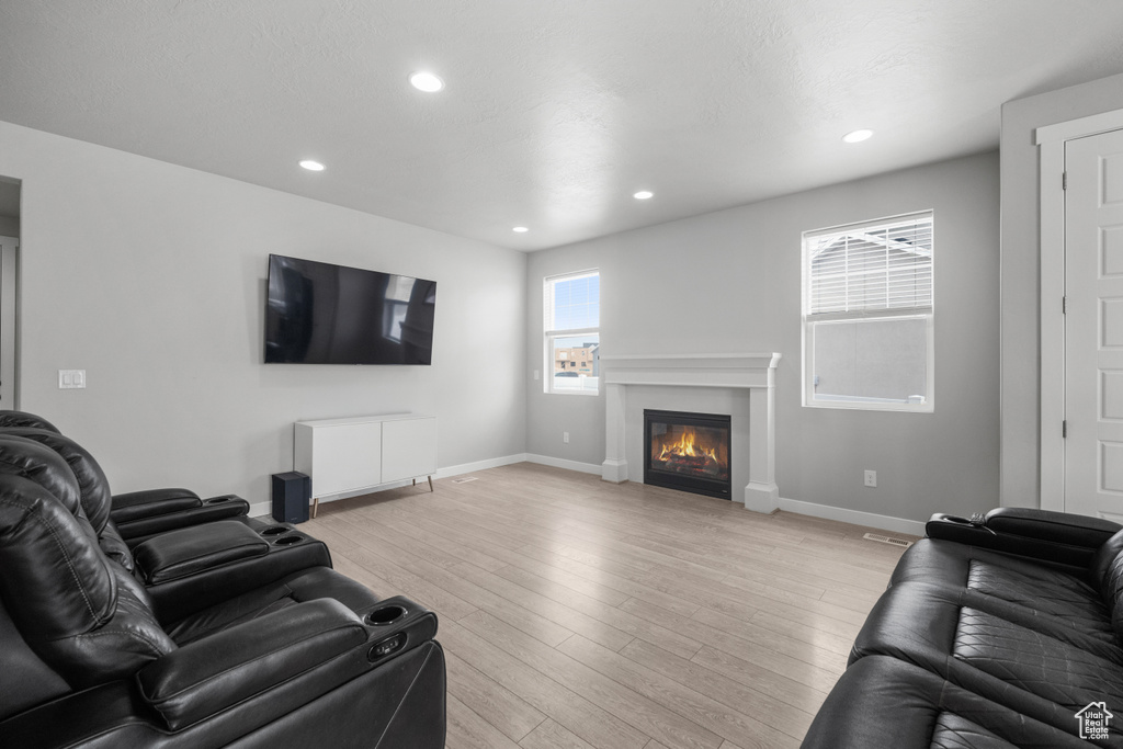 Living area featuring light wood finished floors, a glass covered fireplace, and recessed lighting