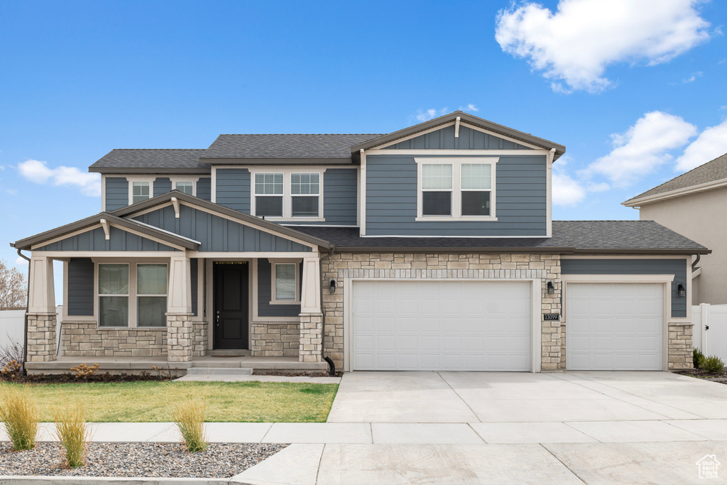 Craftsman inspired home featuring stone siding, board and batten siding, concrete driveway, and roof with shingles