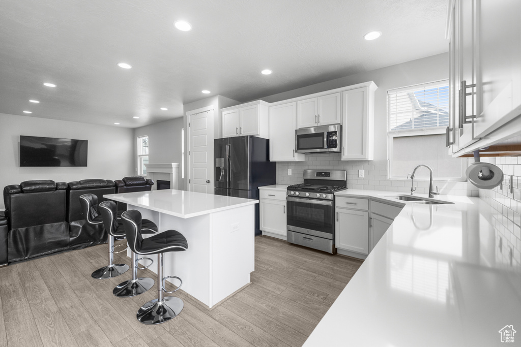Kitchen featuring appliances with stainless steel finishes, a kitchen island, a breakfast bar, wood finished floors, and recessed lighting