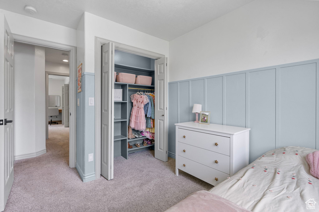 Bedroom featuring a decorative wall, light carpet, a closet, and wainscoting