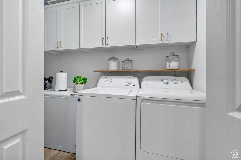 Laundry area with washer and dryer, cabinet space, and wood finished floors