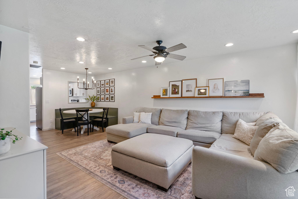 Living area featuring light wood finished floors, a chandelier, a textured ceiling, recessed lighting, and a ceiling fan