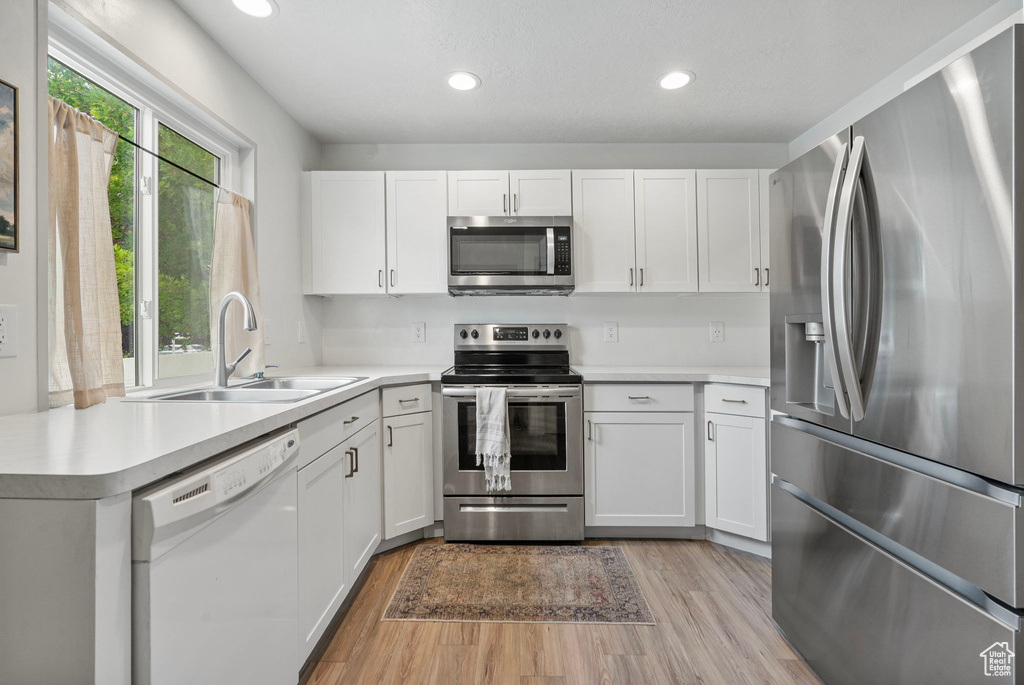 Kitchen with stainless steel appliances, light wood finished floors, light countertops, white cabinetry, and recessed lighting