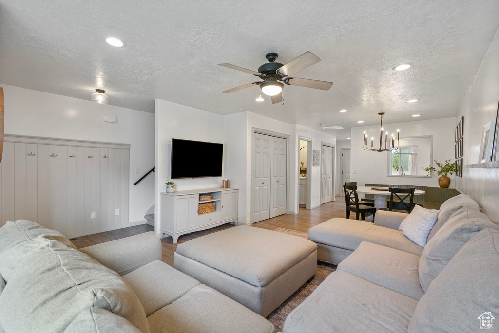 Living room with light wood-style floors, recessed lighting, ceiling fan, a chandelier, and a textured ceiling