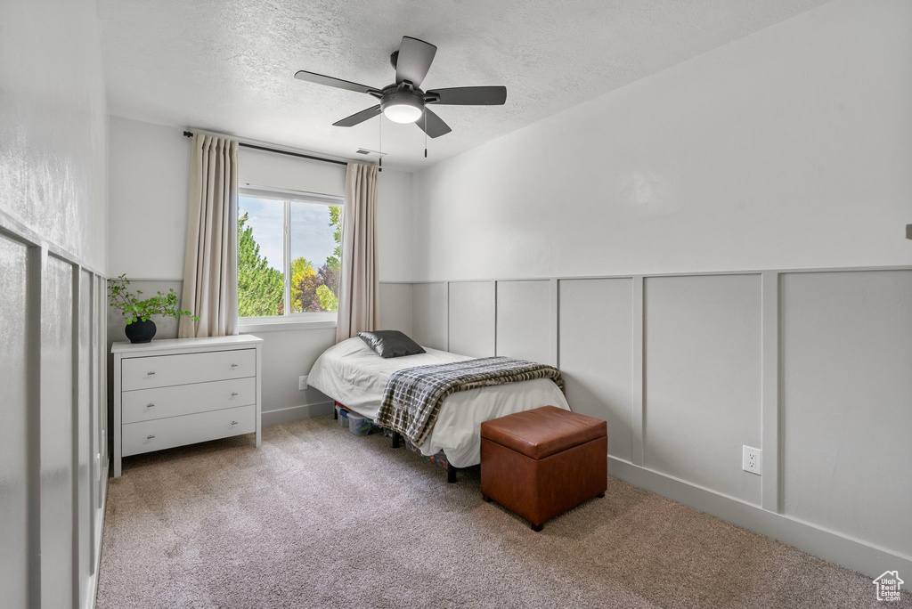Carpeted bedroom with a textured ceiling, a wainscoted wall, and a ceiling fan