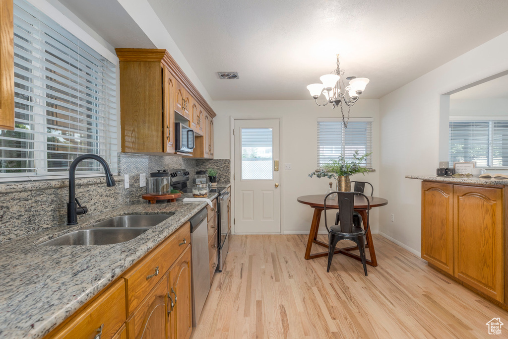 Kitchen featuring brown cabinetry, a chandelier, light wood-style floors, and appliances with stainless steel finishes