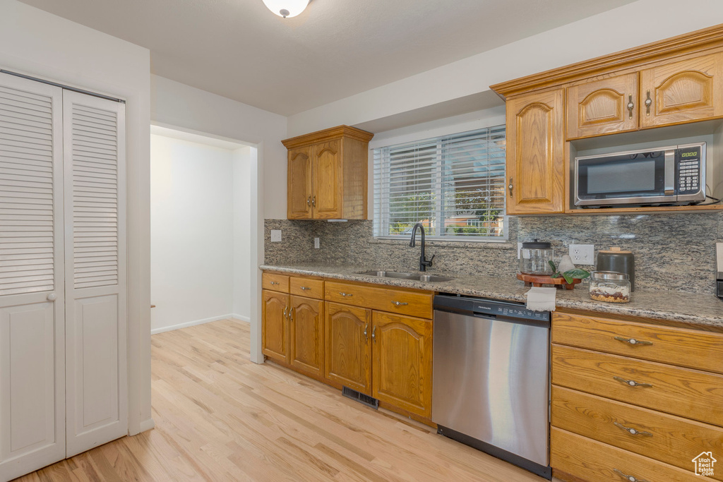 Kitchen with appliances with stainless steel finishes, backsplash, light wood-style flooring, and light stone counters