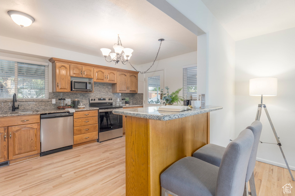 Kitchen with appliances with stainless steel finishes, light wood-style floors, decorative backsplash, a chandelier, and light stone countertops