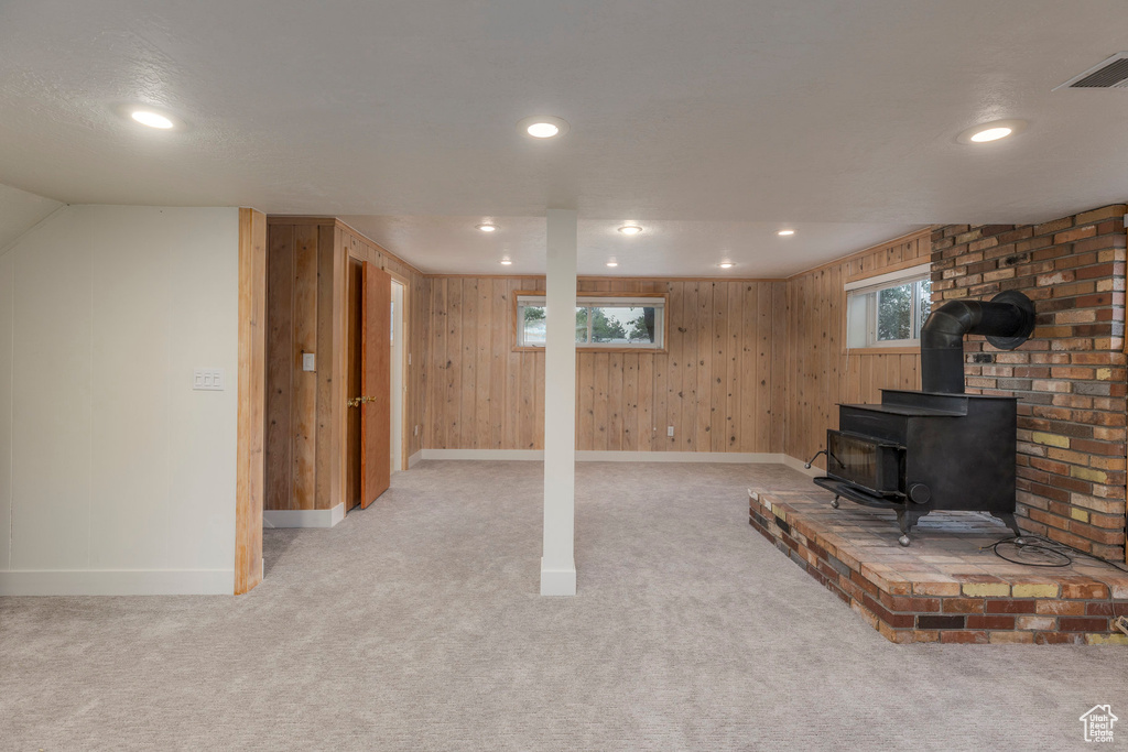 Below grade area featuring light colored carpet, recessed lighting, wood walls, and a wood stove