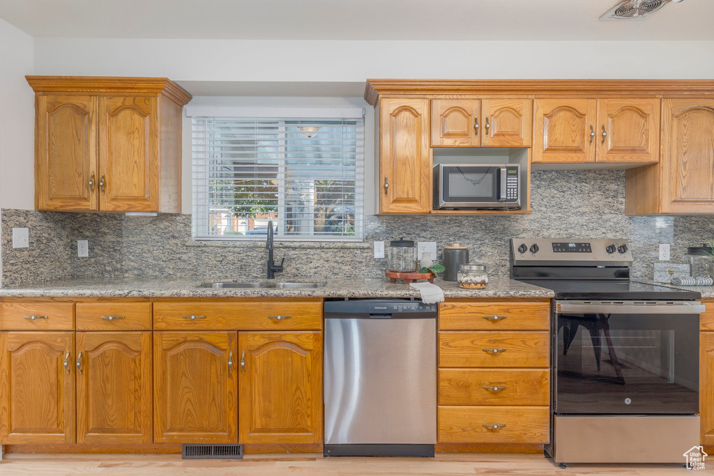 Kitchen with stainless steel appliances, decorative backsplash, light stone counters, and brown cabinetry