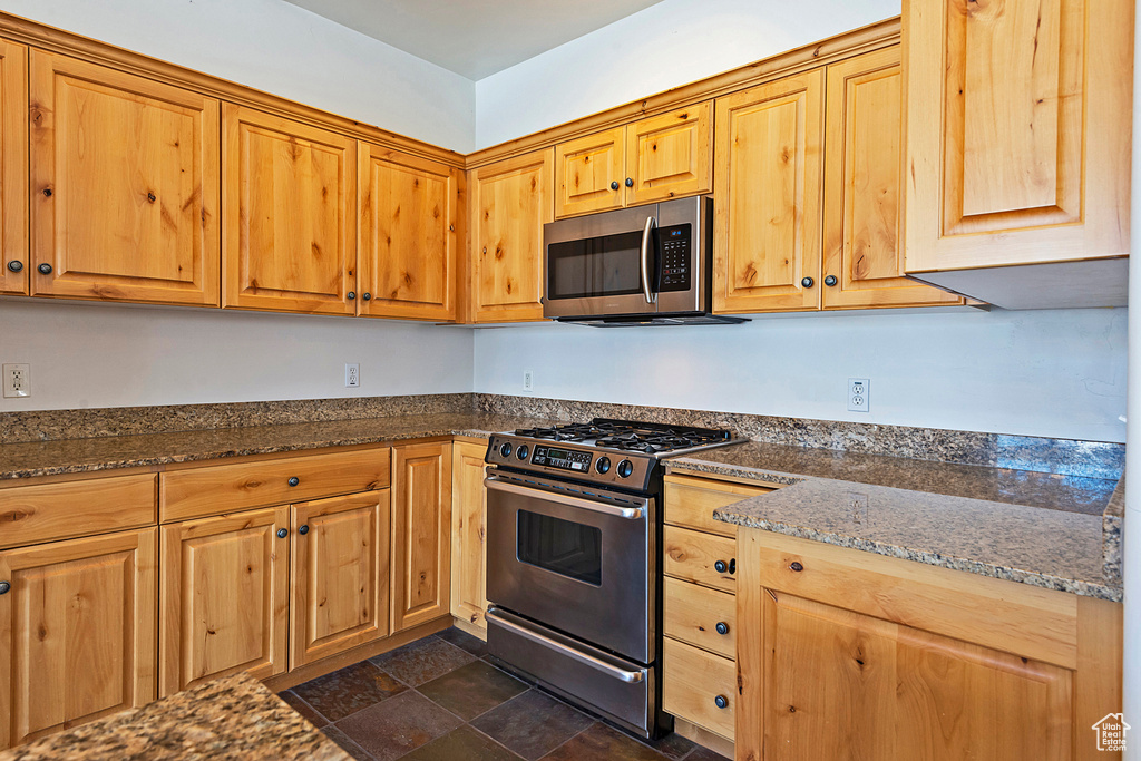 Kitchen with appliances with stainless steel finishes, dark stone counters, and stone finish floors