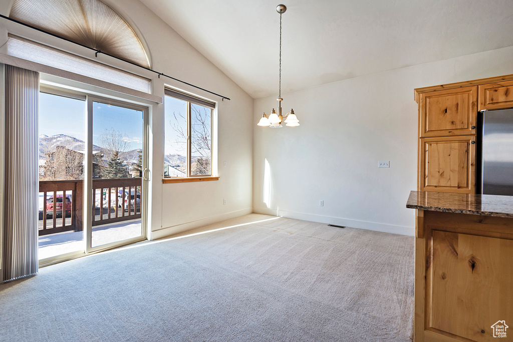 Unfurnished dining area featuring vaulted ceiling, light colored carpet, and a chandelier