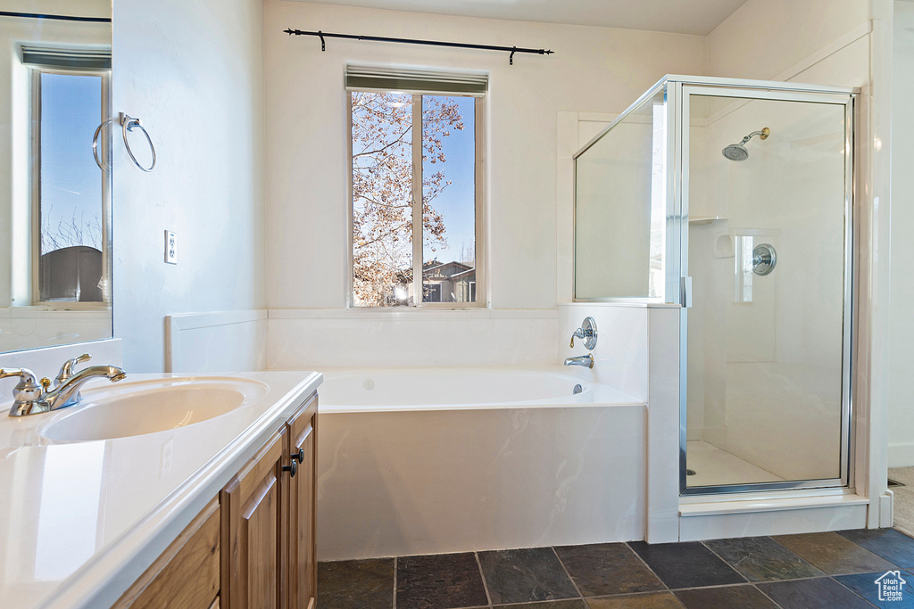 Full bathroom featuring a shower stall, a garden tub, vanity, and stone finish flooring