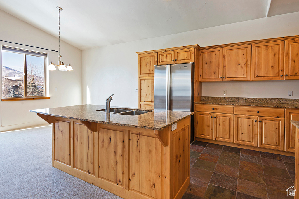 Kitchen featuring freestanding refrigerator, lofted ceiling, dark stone countertops, a chandelier, and hanging light fixtures