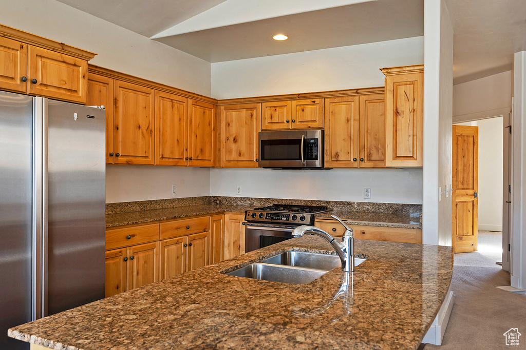 Kitchen with appliances with stainless steel finishes, dark stone countertops, carpet floors, vaulted ceiling, and recessed lighting