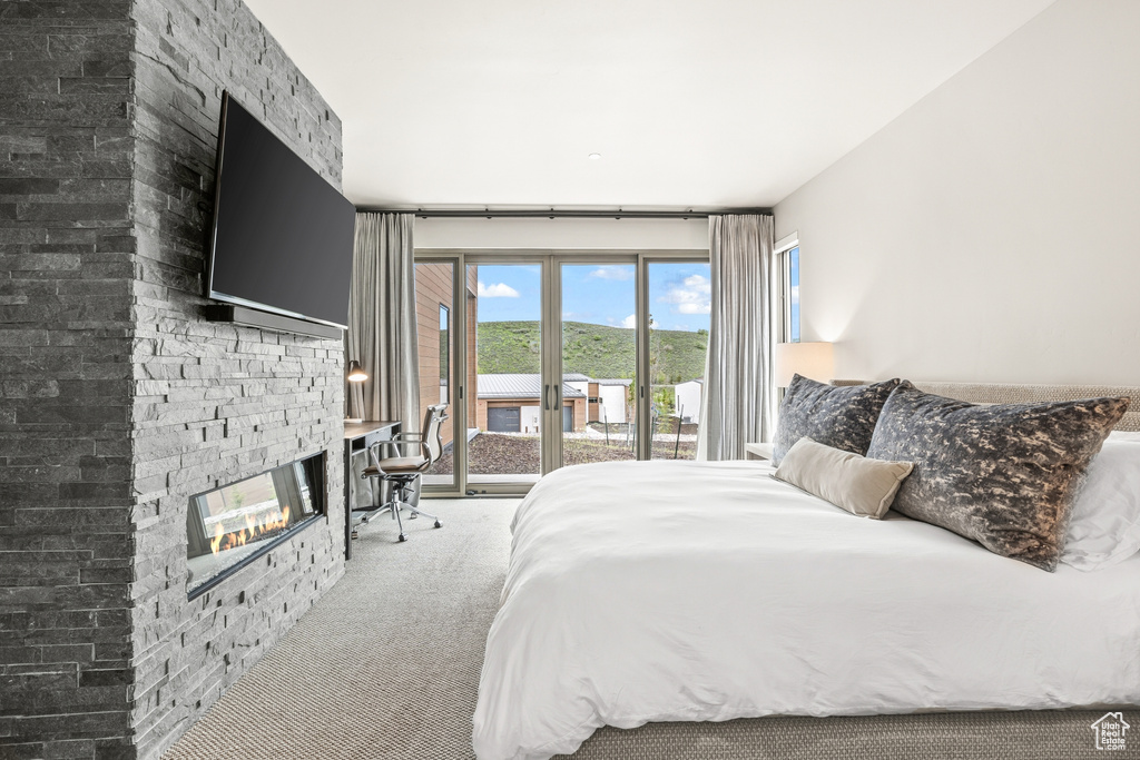 Carpeted bedroom with access to exterior and a stone fireplace