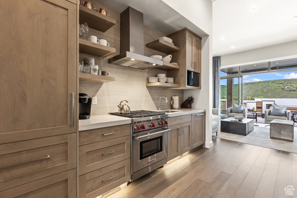 Kitchen featuring open shelves, wall chimney range hood, designer stove, tasteful backsplash, and wood finished floors