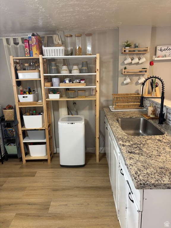Kitchen featuring open shelves, white cabinets, light wood-type flooring, and light stone countertops
