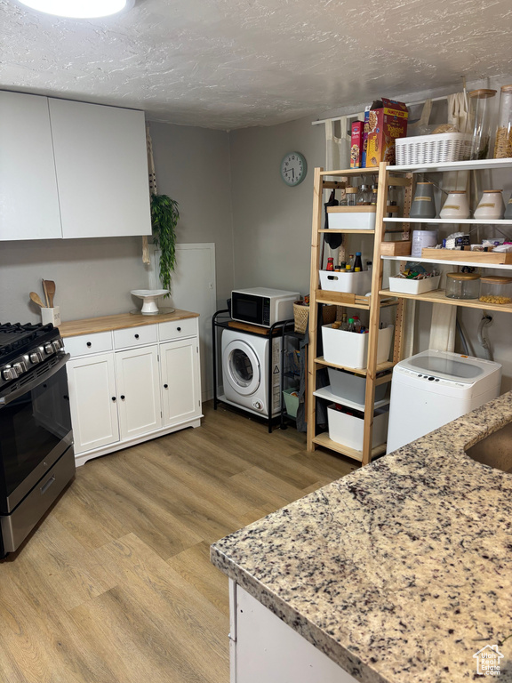 Kitchen featuring stainless steel range with gas cooktop, white cabinetry, light wood-style flooring, washer / clothes dryer, and a textured ceiling