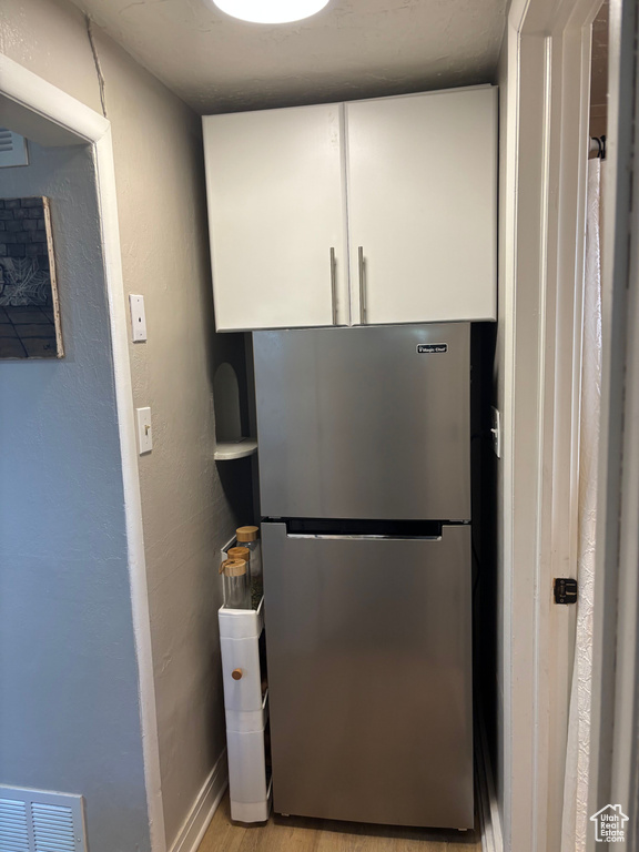 Detailed view of white cabinetry, freestanding refrigerator, and light wood-type flooring