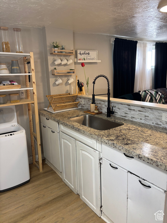 Kitchen with light wood-style flooring, open shelves, washer / clothes dryer, white cabinets, and light stone countertops