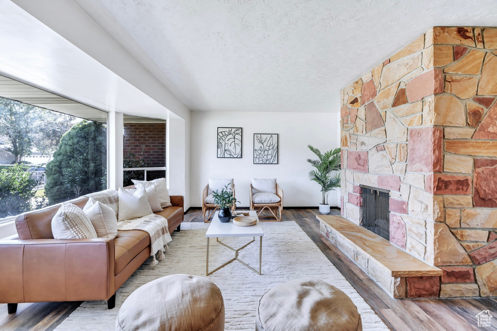 Living area with a stone fireplace, a textured ceiling, and wood finished floors