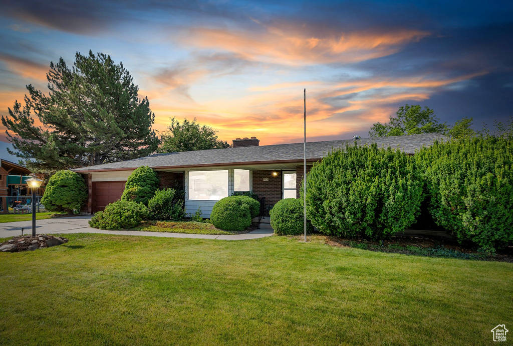 View of front of house with a garage, a chimney, concrete driveway, a front lawn, and brick siding
