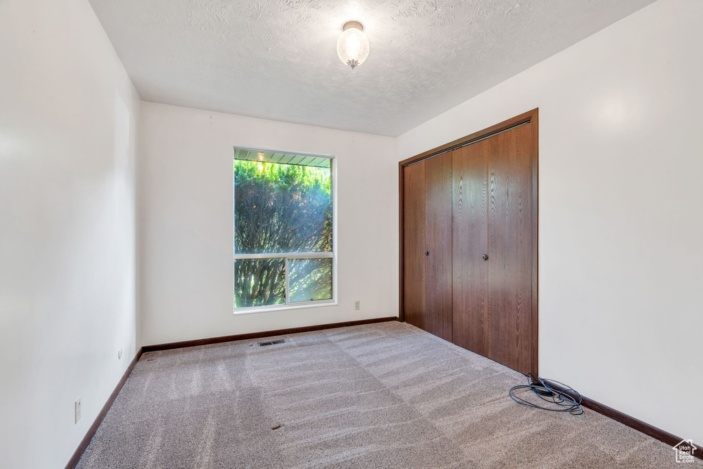 Unfurnished bedroom with carpet, a textured ceiling, and a closet