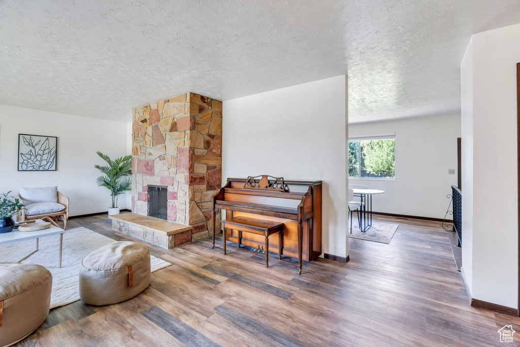 Living area with a textured ceiling, wood finished floors, and a stone fireplace