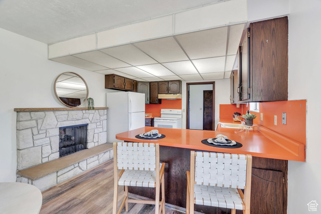 Kitchen with white appliances, a peninsula, light wood-type flooring, a breakfast bar area, and dark brown cabinets