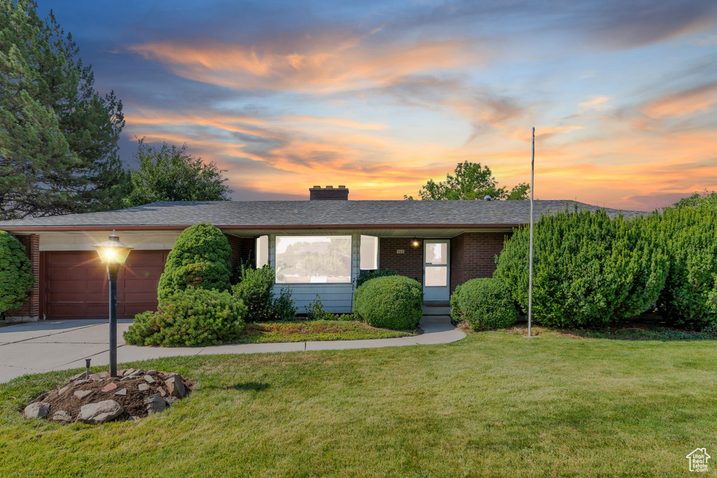 Ranch-style home featuring a lawn, a garage, driveway, a chimney, and brick siding