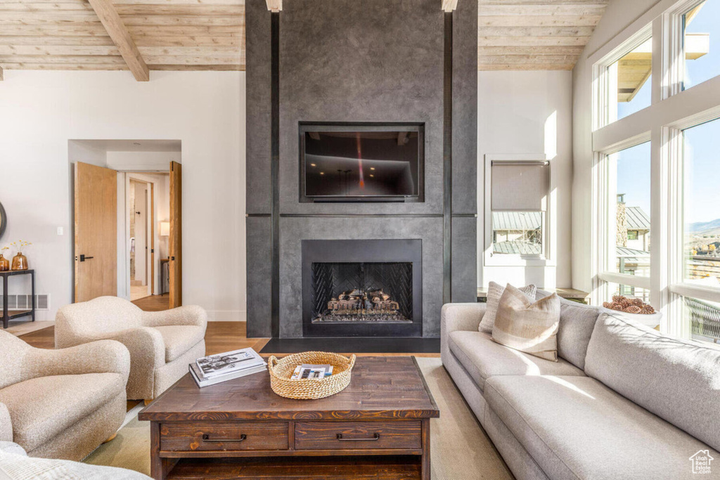 Living room with a wooden ceiling with exposed beams, a fireplace, and wood finished floors