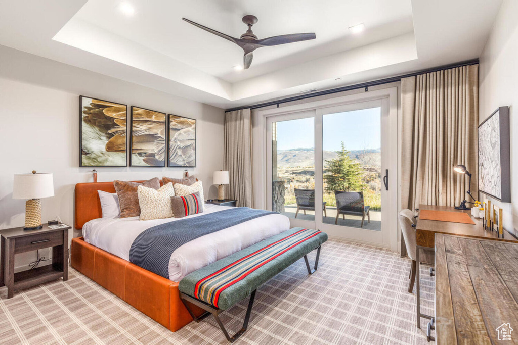 Bedroom with a raised ceiling, access to outside, light colored carpet, and a ceiling fan