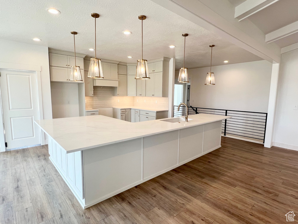 Kitchen with a large island, wood finished floors, tasteful backsplash, recessed lighting, and a textured ceiling